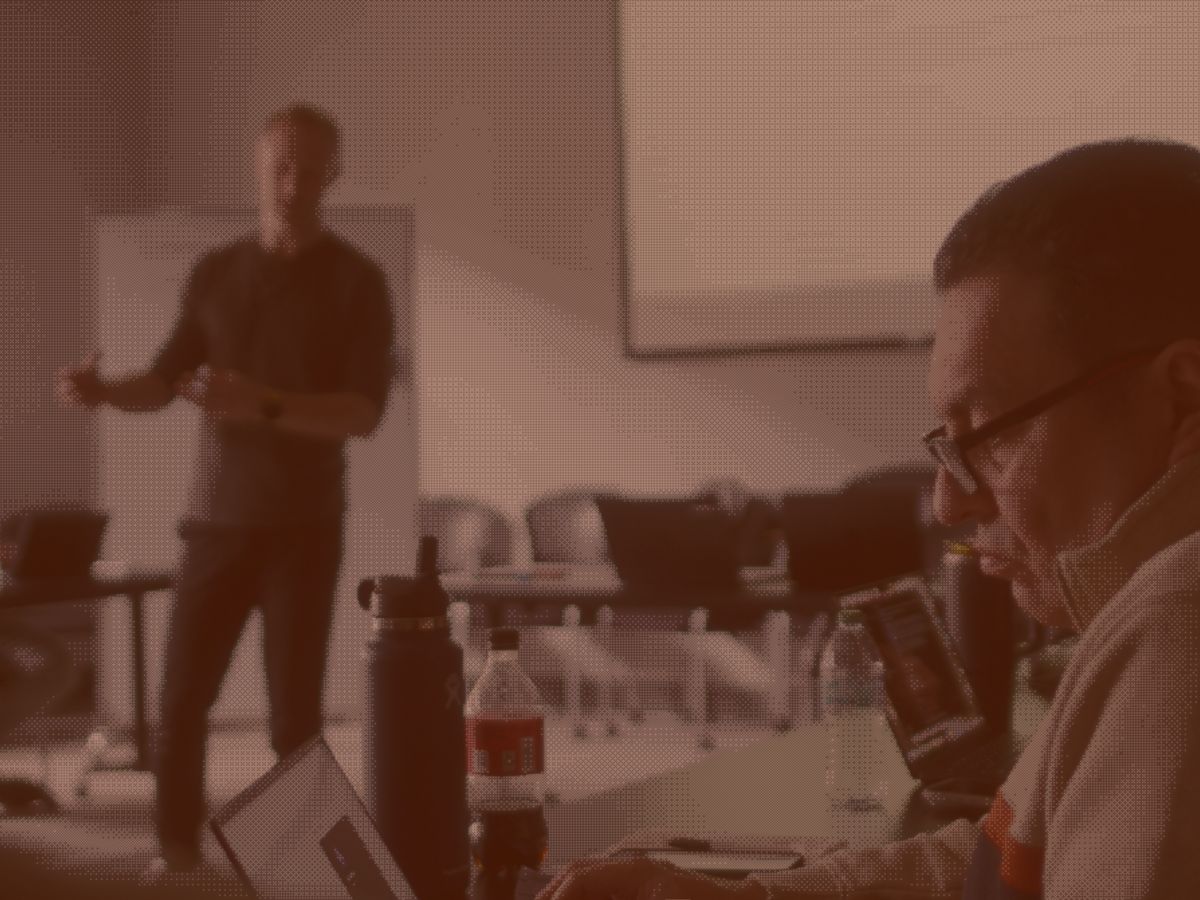 Trainer presenting while employee works on laptop during training day